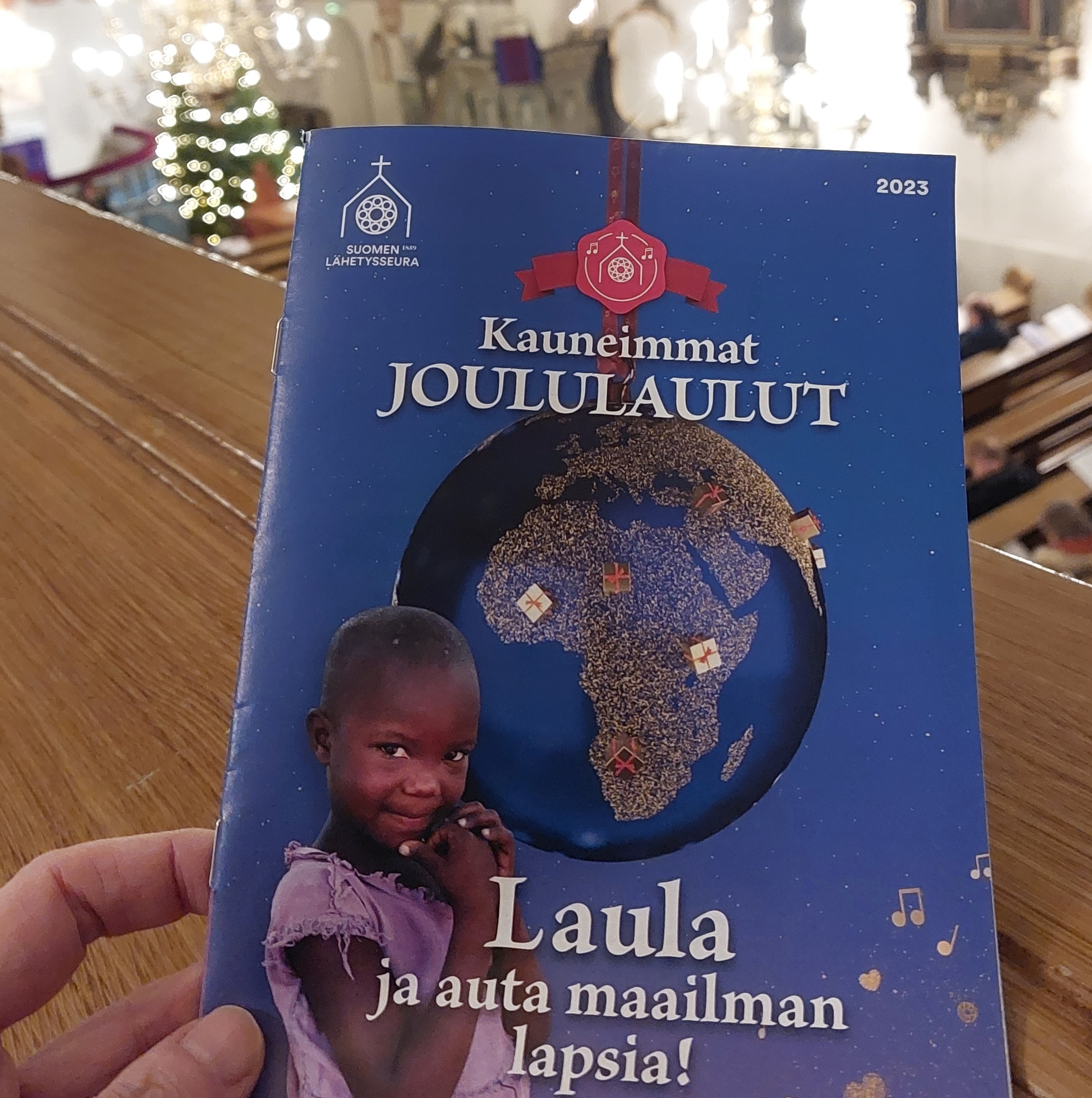 Kauneimmat Joululaulut -lauluvihkon kansi, jossa on lapsi, maapallo ja teksti: Laula ja auta maailman lapsia.