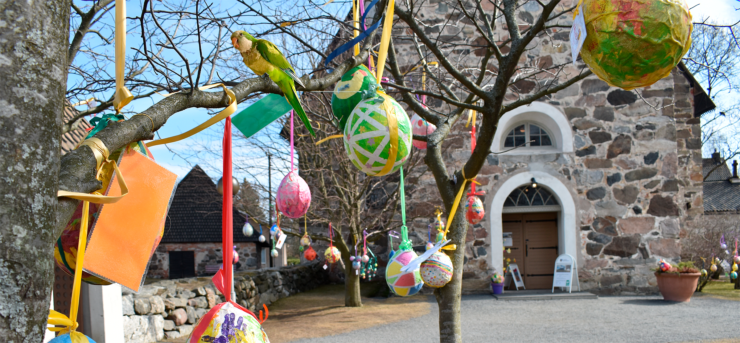 Pääsiäismunia ja vihreä papukaija puussa, taustalla kirkko