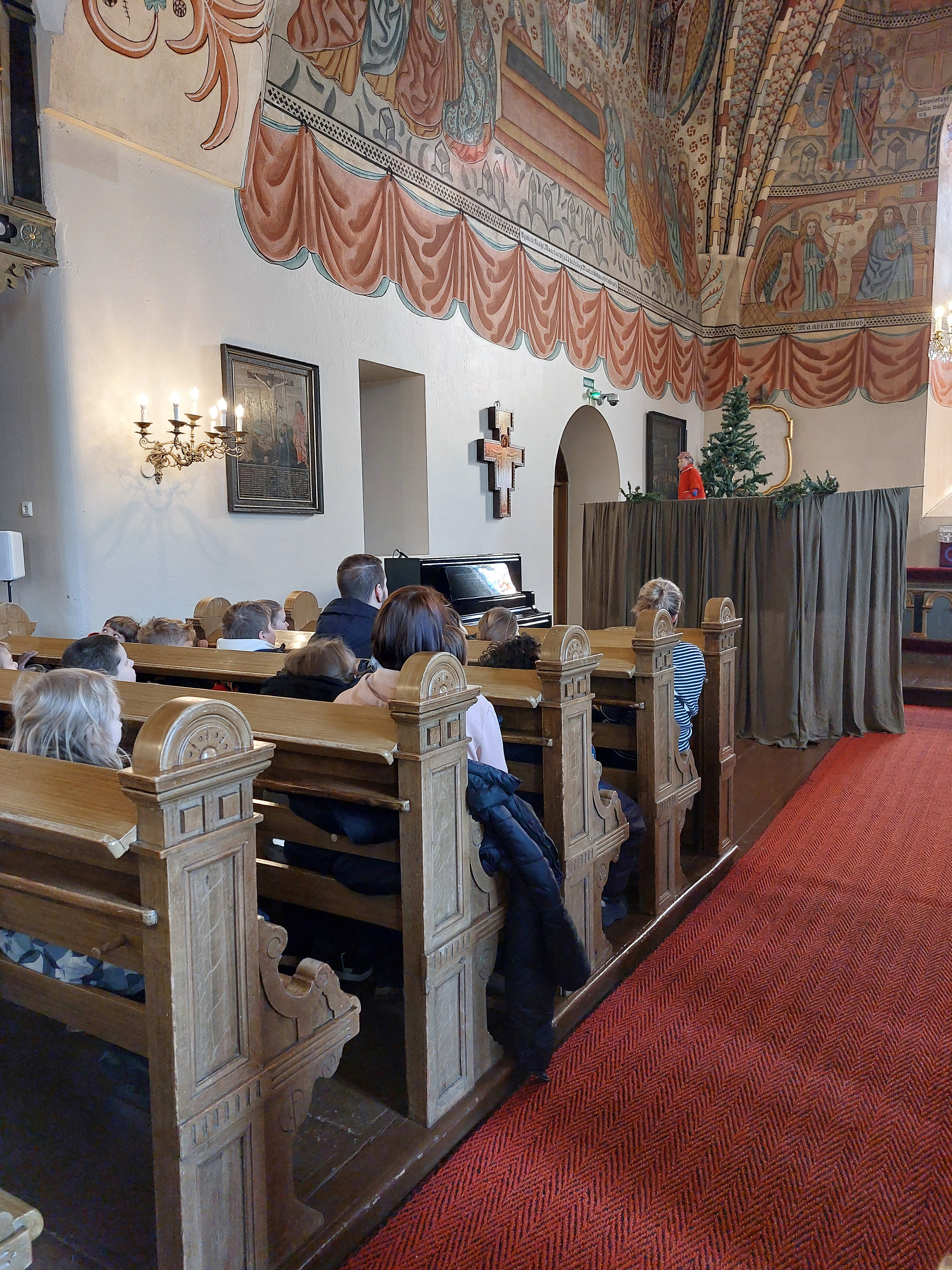 Pyhän Ristin kirkossa ihmisiä kirkonpenkeissä. Kuoriosassa nukketeatteri.