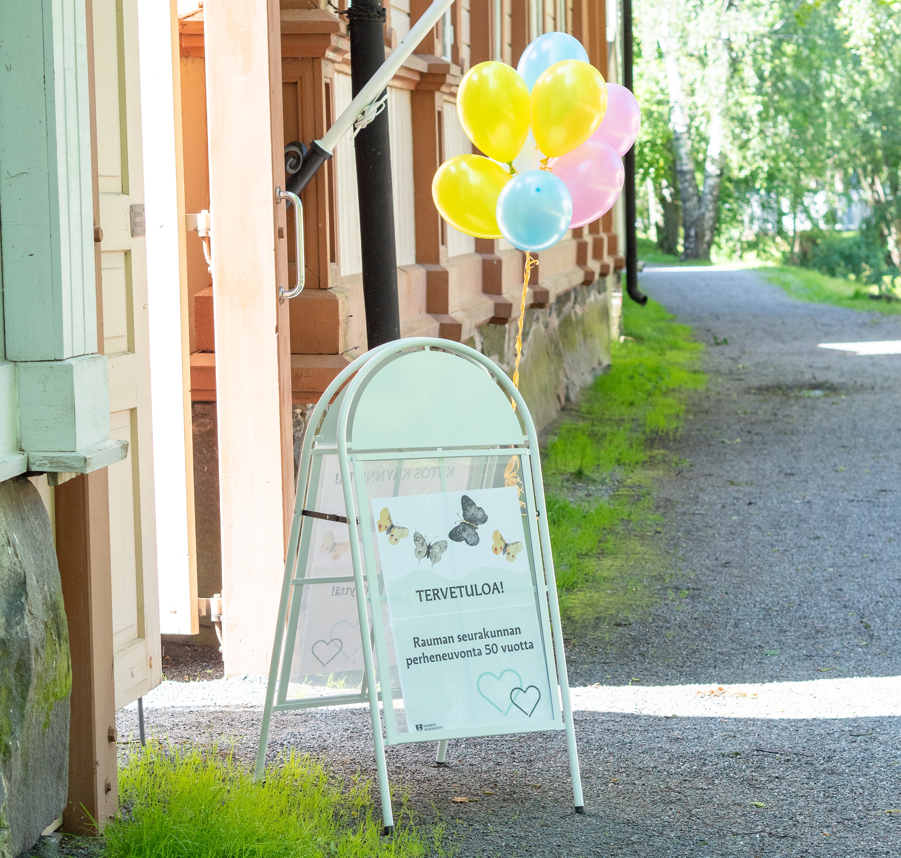 Kuvassa A-ständi ja värikkäitä ilmapalloja talon portilla.