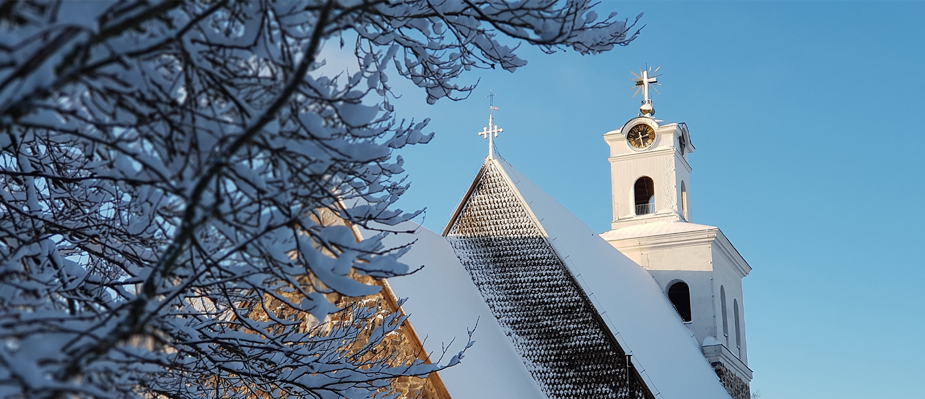Kirkon katto ja torni lumisessa säässä ja sinistä taivasta