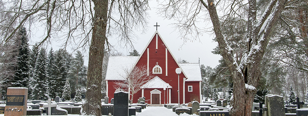 Luminen maisema hautausmaalta, jonka keskellä on punainen puukirkko.