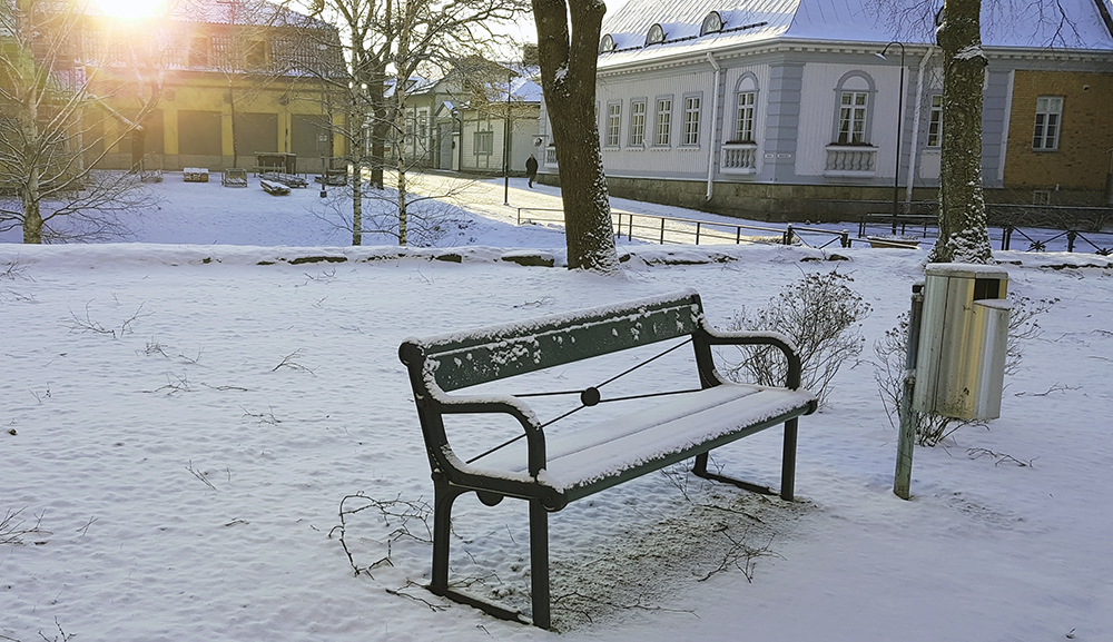 Kirkon pihamaata. Pihalla on lunta, penkki ja valkoinen portti.