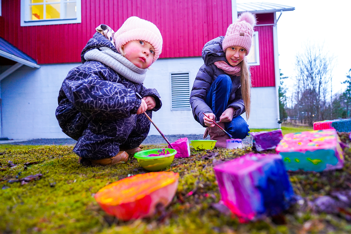 Kaksi lasta kyykyssä maalamassa jääpalikoita talvihaalareissa Unajan seurakuntakodin pihamaalla.