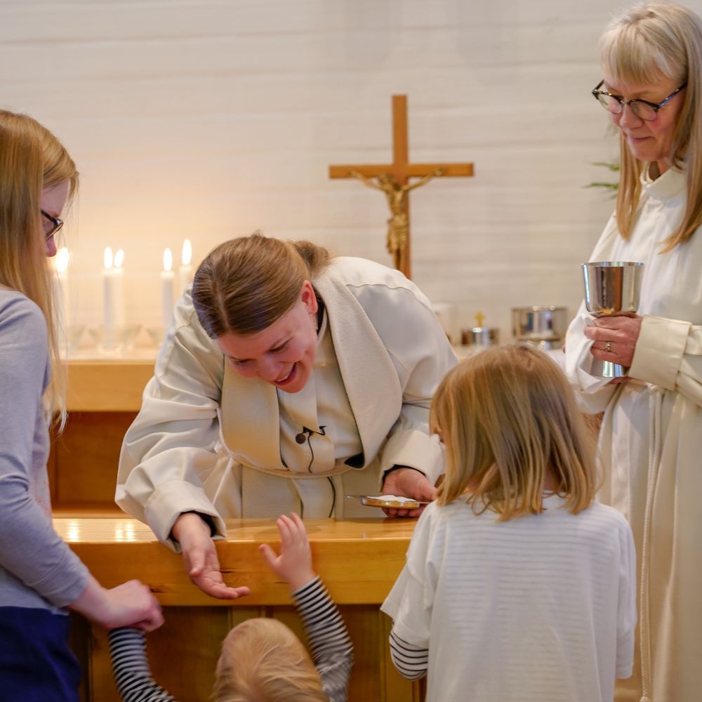 Pappi nojautuu alttarin yli siunaamaan lapsen