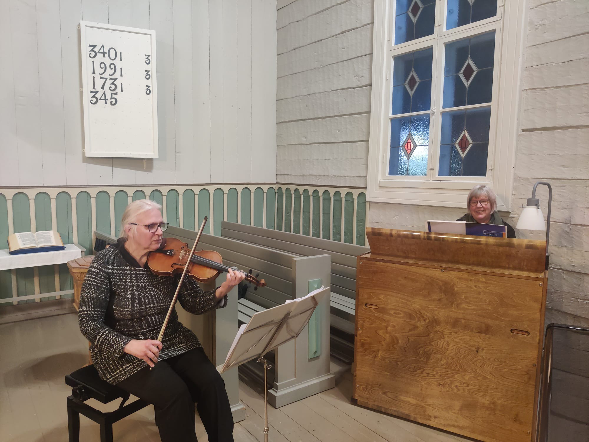 Sisäkuva kirkosta. Nainen soittaa viulua ja taka-alalla nainen urkuharmoonin takana.